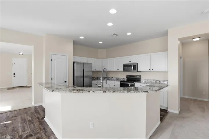 Kitchen featuring light stone counters, stainless steel appliances, white cabinets, a spacious island, and recessed lighting