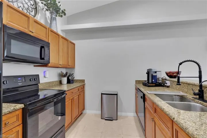Kitchen featuring black appliances, light stone counters, vaulted ceiling, a peninsula, and recessed lighting