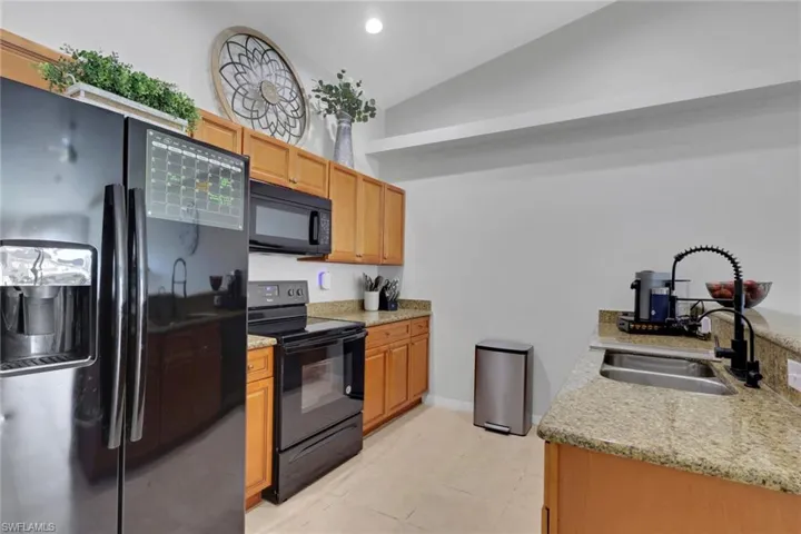 Kitchen with black appliances, light stone counters, and lofted ceiling