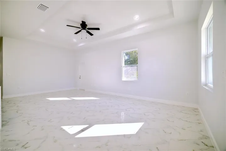 Empty room with a tray ceiling, light marble finish flooring, recessed lighting, and a ceiling fan