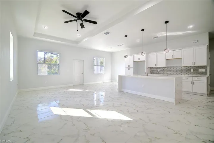 Unfurnished living room with light marble finish flooring, ceiling fan, recessed lighting, and a raised ceiling