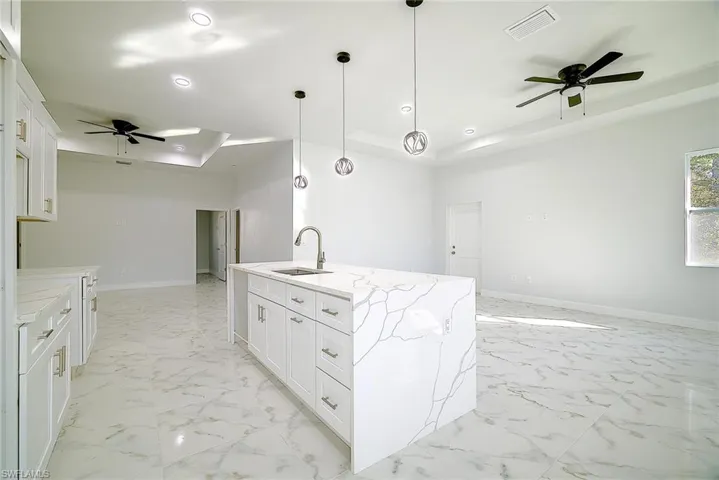 Kitchen featuring a ceiling fan, a tray ceiling, open floor plan, white cabinets, and recessed lighting