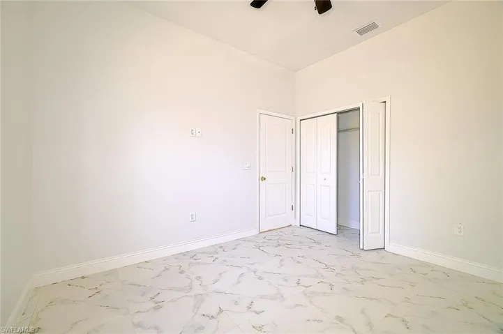 Unfurnished bedroom featuring light marble finish flooring, ceiling fan, and a closet