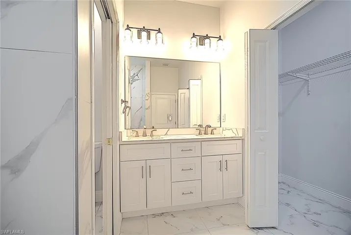 Full bath with light marble finish floors, double vanity, and a spacious closet