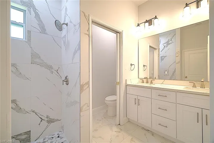 Full bath with double vanity, light marble finish flooring, and a marble finish shower