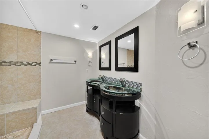 Bathroom featuring a dual vanity with glass vessel sinks, coordinating black framed mirrors, and contemporary wall sconces