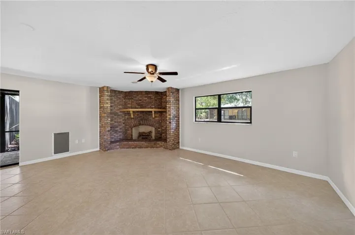 Spacious room featuring a brick fireplace with a wood mantle, tile flooring, a ceiling fan, and a window providing natural light