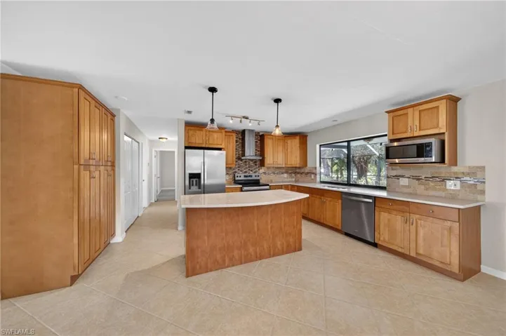 Spacious kitchen featuring an island with pendant lighting, stainless steel appliances, ample cabinetry, stone countertops, and a decorative tile backsplash