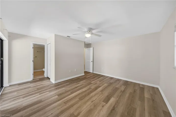 Spacious room featuring wood-finish flooring, a ceiling fan with integrated lighting, a window, and a door opening into an adjacent space