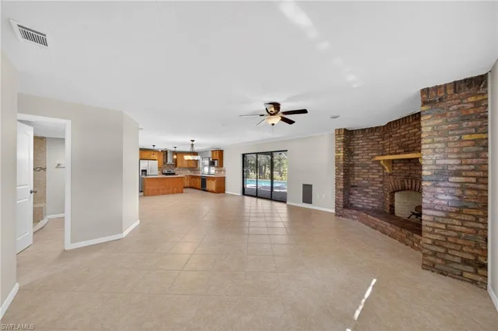 Spacious living area featuring tile flooring, a brick-surround fireplace with a wood mantle, and a ceiling fan