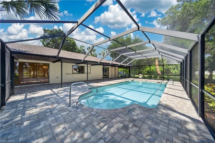 Screened swimming pool enclosure featuring a rectangular pool with integrated steps, a paver deck, and surrounding exterior building