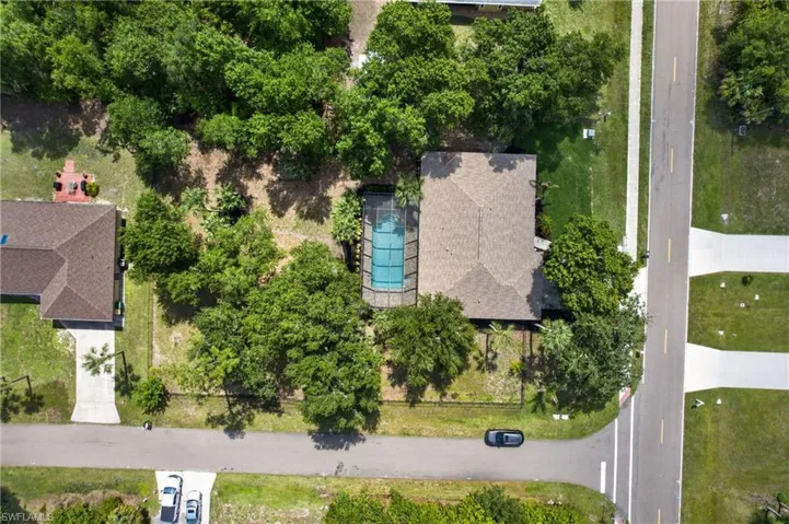 Aerial view showcasing a property featuring a pool, mature trees, and a street-facing driveway
