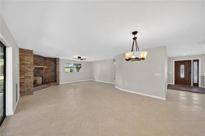 Spacious living area featuring neutral wall tones, tile flooring, a brick fireplace with a wood mantle, and a ceiling fan