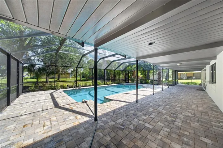 Screened lanai featuring a swimming pool, extensive paver decking, and a covered patio area with a slatted ceiling