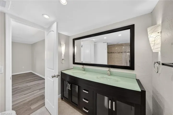 Bathroom vanity featuring dual vessel sinks, a glass countertop, and dark wood cabinetry with chrome hardware