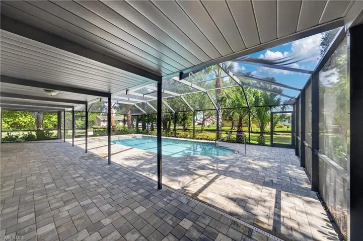 Screened outdoor living area featuring a rectangular pool and expansive paver decking