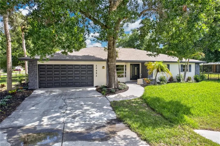 Single-story residence featuring a two-car garage with stone-clad accents, a curved concrete pathway, mature trees, and a manicured lawn