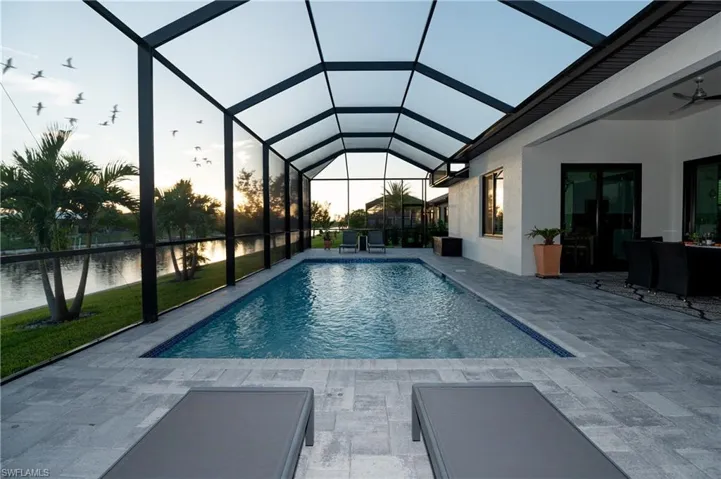 View of swimming pool featuring a lanai, ceiling fan, a water view, and a patio