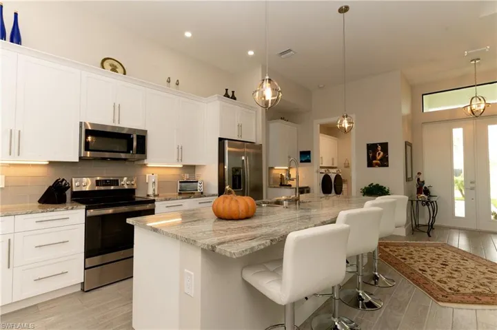 Kitchen with appliances with stainless steel finishes, sink, a center island with sink, washing machine and dryer, and white cabinetry