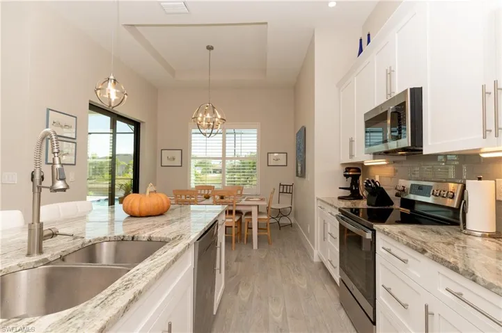 Kitchen with stainless steel appliances, sink, decorative light fixtures, light hardwood / wood-style floors, and white cabinetry