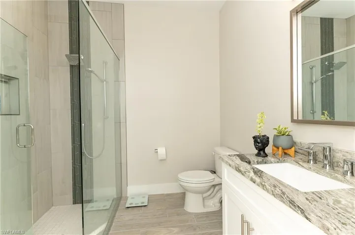 Bathroom with hardwood / wood-style floors, vanity, toilet, and a shower with shower door