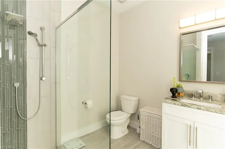 Bathroom featuring hardwood / wood-style flooring, vanity, toilet, and tiled shower