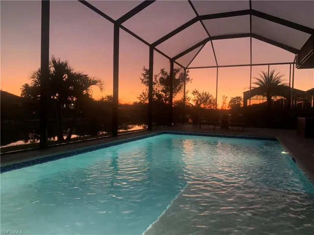 Pool at dusk featuring a lanai and a patio