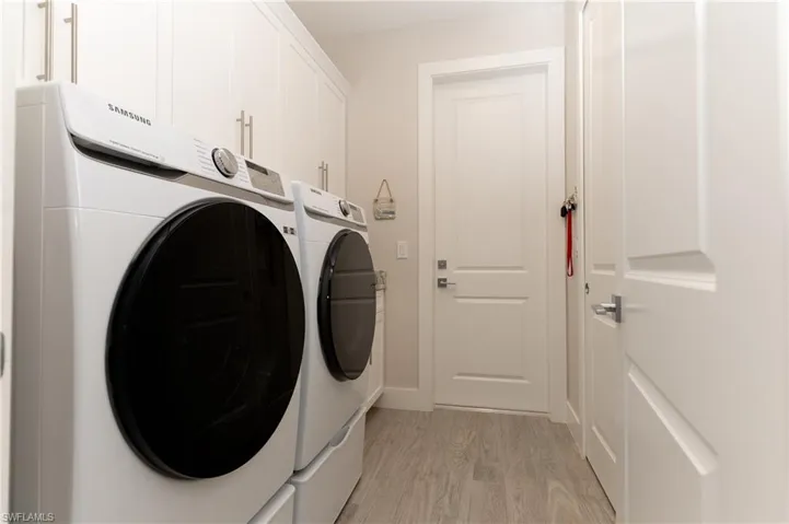 Laundry area with cabinets, washing machine and dryer, and light hardwood / wood-style floors