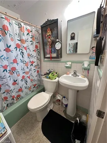 Bathroom featuring shower / tub combo with curtain, tile walls, speckle patterned floor, and wainscoting