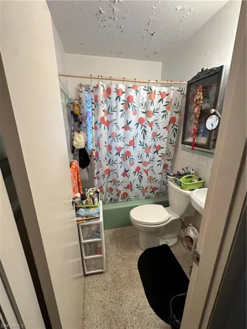 Bathroom with shower / tub combo, tile walls, speckled floor, and a textured ceiling
