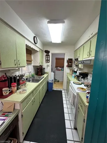 Kitchen with stove, light tile patterned floors, light countertops, and green cabinetry