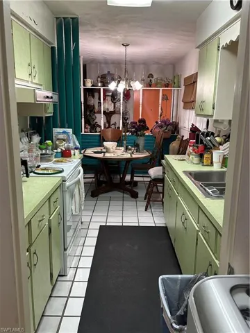 Kitchen with light countertops, green cabinets, light tile patterned flooring, stove, and a chandelier