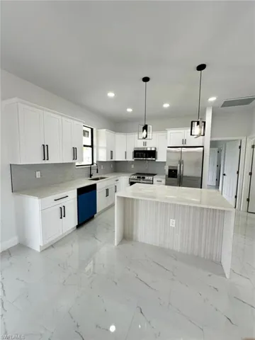Kitchen featuring appliances with stainless steel finishes, a center island, a sink, baseboards, and recessed lighting