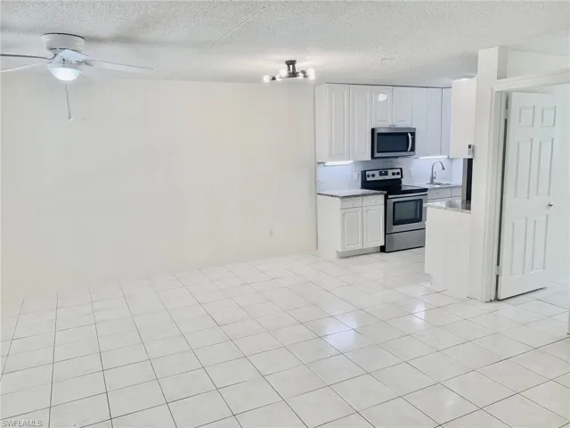 Kitchen featuring stainless steel appliances, white cabinetry, a textured ceiling, light stone countertops, and light tile patterned flooring