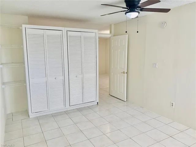 Unfurnished bedroom featuring a ceiling fan, a textured ceiling, light tile patterned floors, and two closets