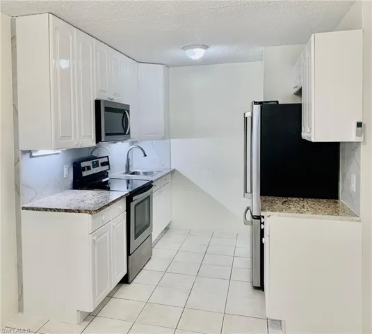 Kitchen featuring appliances with stainless steel finishes, a textured ceiling, light stone counters, tasteful backsplash, and white cabinets