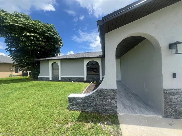 View of exterior entry featuring a yard and central air condition unit