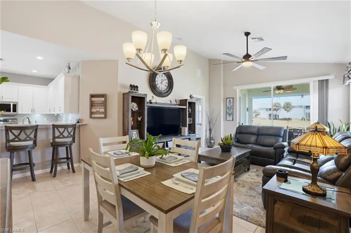 Dining room with light tile patterned flooring, a chandelier, vaulted ceiling, and ceiling fan
