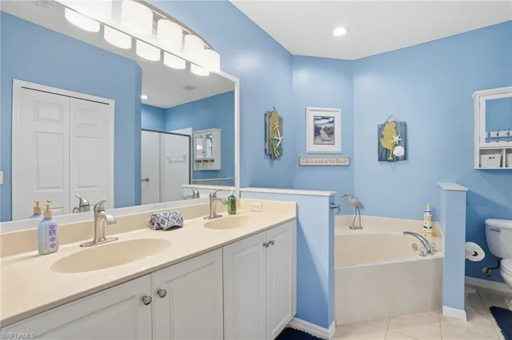 Bathroom with a bath, light tile patterned floors, a shower stall, double vanity, and a closet