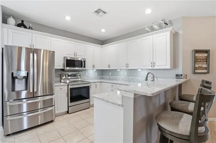 Kitchen with appliances with stainless steel finishes, light stone counters, white cabinets, a peninsula, and light tile patterned floors