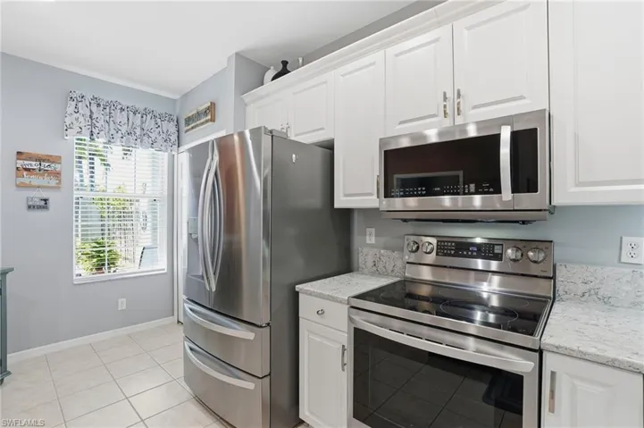 Kitchen with appliances with stainless steel finishes, white cabinetry, light tile patterned flooring, and light stone countertops