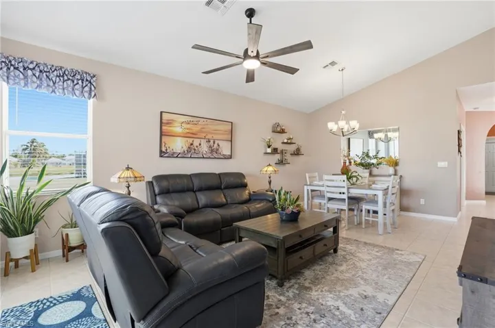 Living room with light tile patterned flooring, ceiling fan, a chandelier, healthy amount of natural light, and high vaulted ceiling