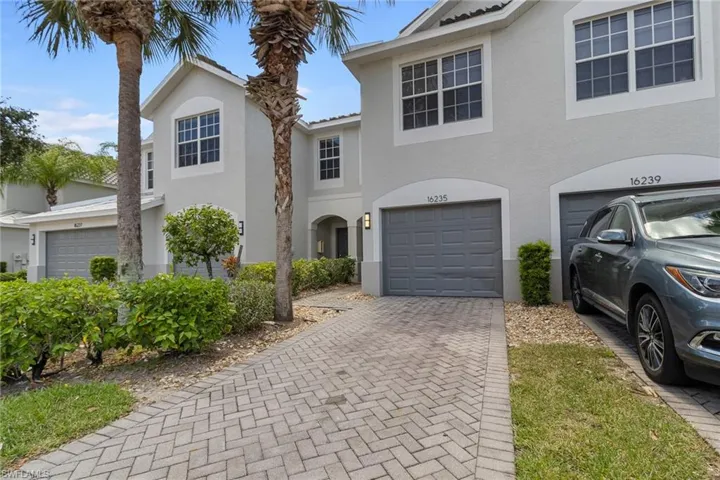 Stucco exterior with multiple windows, paver driveway, attached garage, and mature palm trees