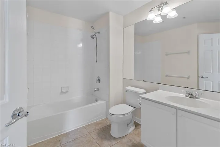 Bathroom featuring a full-size bathtub with white tile surround, a single vanity with an integrated sink, a large wall-mounted mirror, and tile flooring