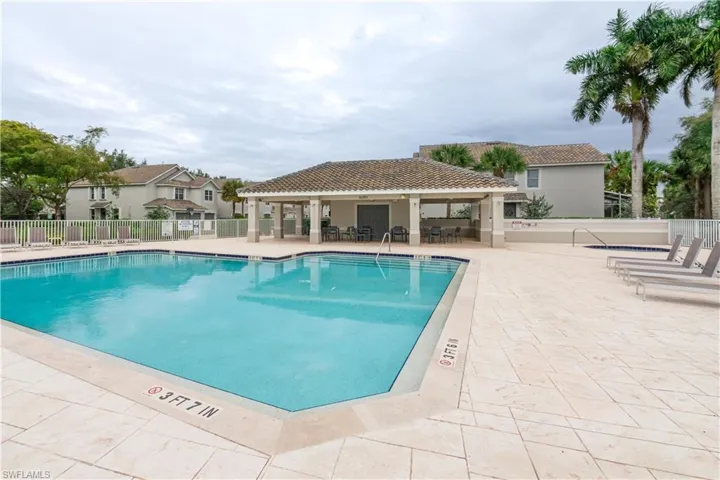 Community swimming pool with a tiled deck, covered patio, and adjacent hot tub, surrounded by mature palm trees