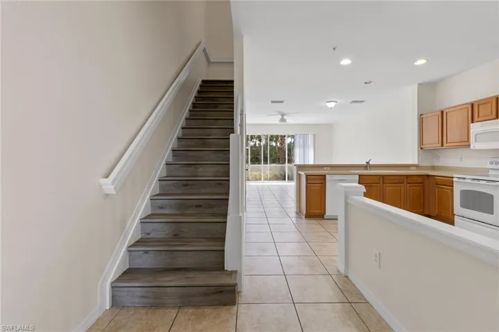 Wood-finish stairs with white risers, tiled flooring, wood cabinetry, built-in kitchen appliances, and a ceiling fan
