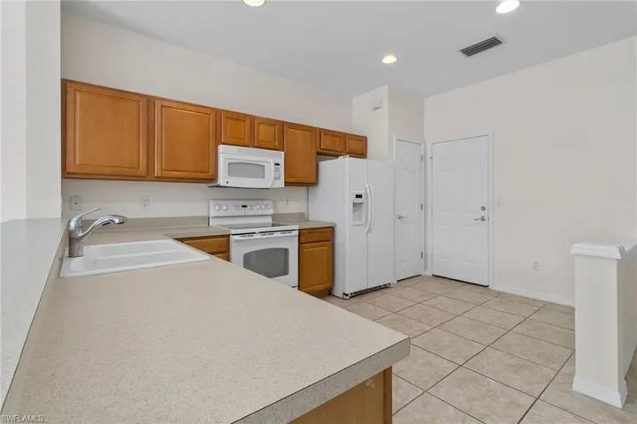 Kitchen featuring wood cabinetry, white appliances, light-toned countertops, and tiled flooring