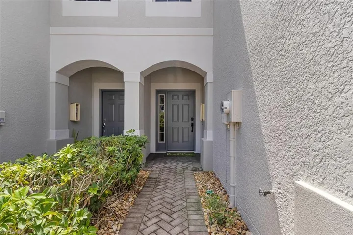 Stucco exterior with arched entryway, brick paver walkway, and planted landscaping