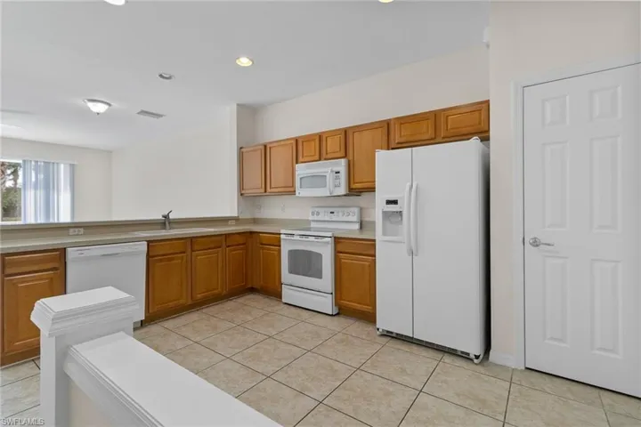Kitchen featuring wood-finish cabinetry, tile flooring, white appliances, and a pass-through counter