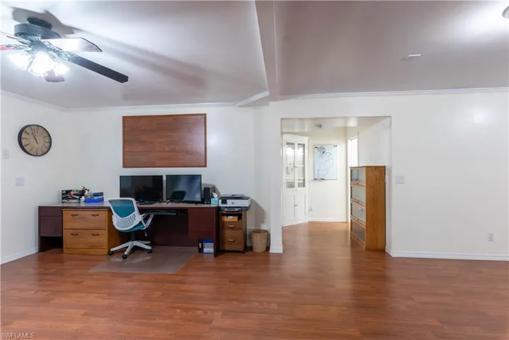 Home office featuring dark wood-type flooring, ceiling fan, and crown molding